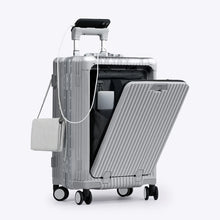 Load image into Gallery viewer, Angled front view of the silver colored carry-on with the front panel opened. It is arranged with a charging cellphone, a small purse, and a laptop in its compartment. 
