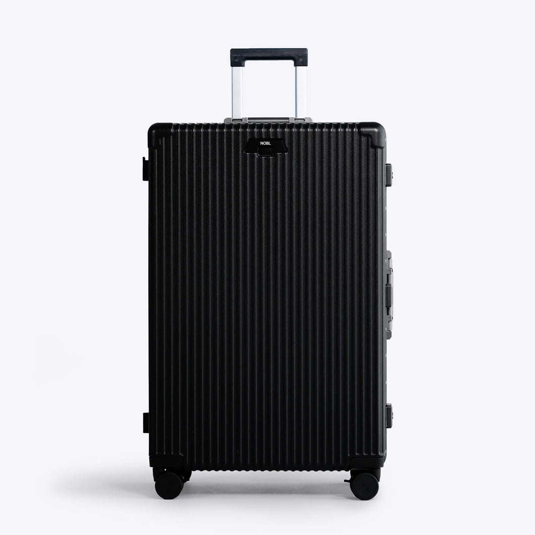 Front panel view of the large black suitcase with silver colored accents. The telescopic handle is partly extended. 