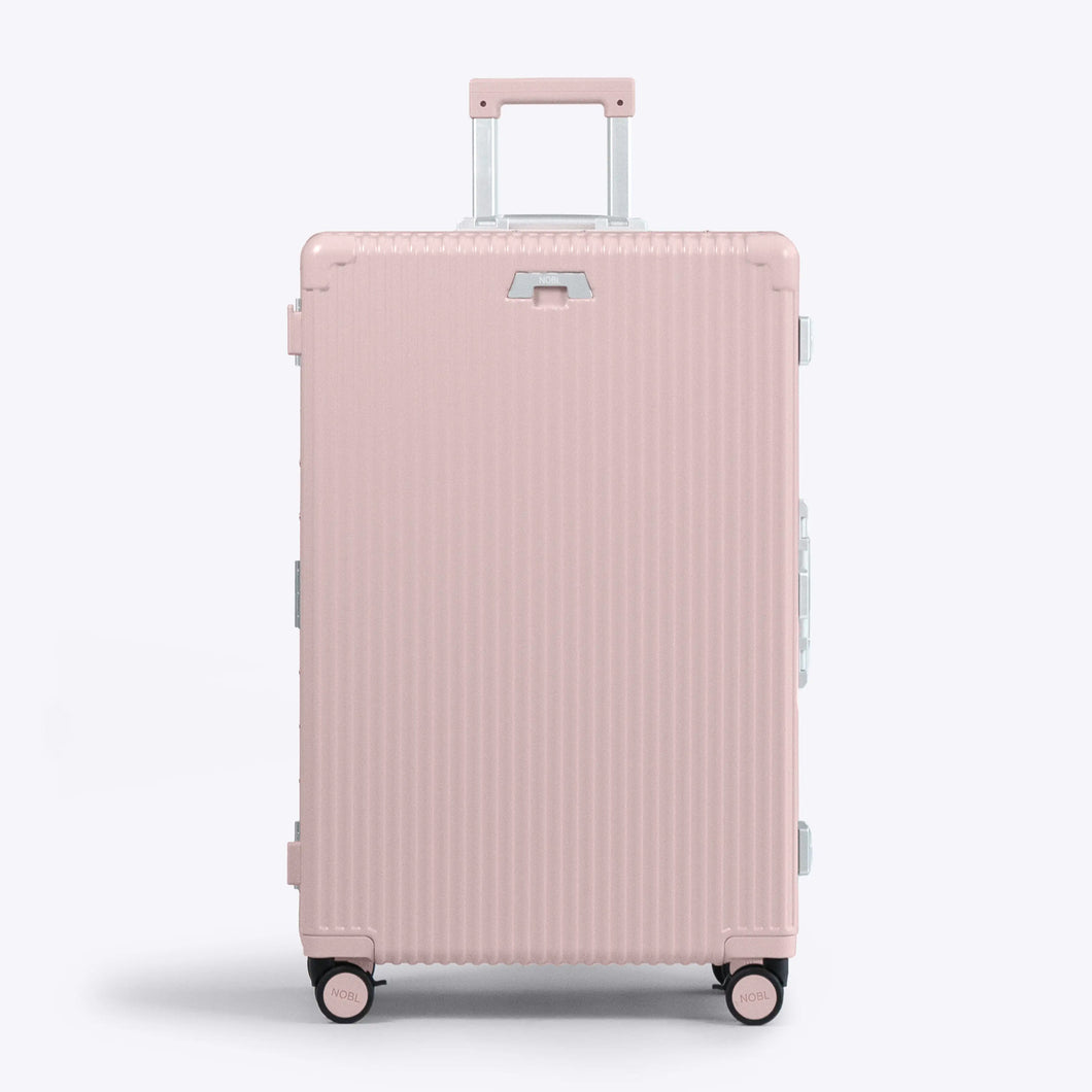Front panel view of the large pink suitcase with silver-colored accents. The telescopic handle is extended. 