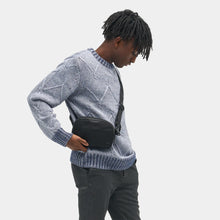 Load image into Gallery viewer, A young man carrying the black sling bag across his torso.
