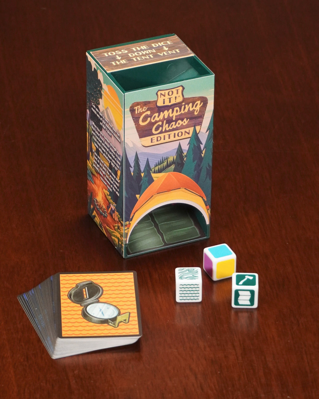 Angled view of the box with the box, cards, and three dice arranged on a table. 