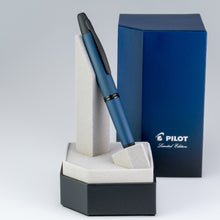 Load image into Gallery viewer, The pen placed on its stand with the packaging in the background.
