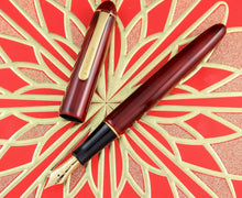 Load image into Gallery viewer, Front view of the Fountain Pen. The cap has been removed and is placed on the side. The grip section is revealed to be black in color and with a golden ring connecting it to the barrel. The nib is also golden in color.
