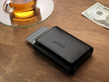 Load image into Gallery viewer, Angled view of the closed Pularys Boston wallet in black on a brown wooden table. The credit cards are peeking from the compartment. A glass tea cup is behind the wallet, and next to it, a $20 bill.  
