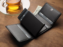 Load image into Gallery viewer, Angled view of the Pularys Boston wallet in black on a brown wooden table. A $20 bill and credit cards are peeking from the compartments. A glass tea cup is behind the wallet.  
