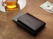 Load image into Gallery viewer, Angled view of the closed Pularys Boston wallet in brown on a brown wooden table. The credit cards are peeking from the compartment. A glass tea cup is behind the wallet, and next to it, a $20 bill.  
