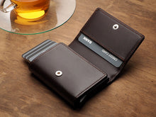 Load image into Gallery viewer, Angled view of the opened Pularys Boston wallet in brown on a brown wooden table. A glass tea cup is behind the wallet.  
