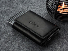 Load image into Gallery viewer, Angled view of the closed Pularys Colorado RFID black leather wallet. Set on a gray textured surface with a candle set next to it.
