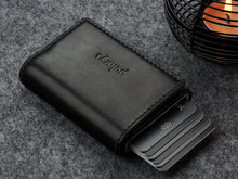 Load image into Gallery viewer, Angled view of the closed Pularys Colorado RFID black leather wallet. Six credit cards are peeking from the compartment. Set on a gray textured surface with a candle set next to it.
