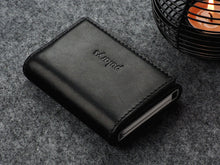 Load image into Gallery viewer, Angled view of the closed Pularys Colorado RFID black leather wallet. Set on a gray textured surface with a candle set next to it.
