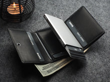 Load image into Gallery viewer, The opened Pularys Colorado RFID Wallet in black on a textured gray surface. The compartments have credit cards, and a $20 bill. A candle is set behind at the corner of the image.
