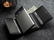 Load image into Gallery viewer, The opened Pularys Colorado RFID Wallet in black on a textured gray surface. The compartments have credit cards, and a $20 bill. A candle is set behind at the corner of the image.
