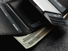 Load image into Gallery viewer, Close up to the The opened Pularys Colorado RFID Wallet in black on a textured gray surface. The cash compartment has a $20 bill, and a set of credit cards are placed in the compartments. 
