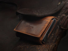Load image into Gallery viewer, Angled view of the brown wallet a top a saddle. 
