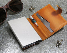 Load image into Gallery viewer, Interior view of the cognac leather wallet arranged with a pen, credit card, sun glasses and jax toys. 
