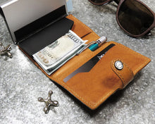 Load image into Gallery viewer, Interior view of the cognac wallet arranged with a pen, a 100 dollar bill, a credit card, and sunglasses. 
