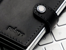 Load image into Gallery viewer, Close up to the pularys logo embossing on the black wallet atop a white keyboard. 
