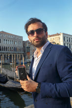 Load image into Gallery viewer, A young man holding a black wallet in an urban setting. 
