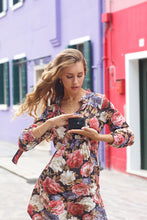 Load image into Gallery viewer, A young woman holding a black wallet in an urban setting. 

