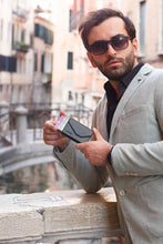 Load image into Gallery viewer, A young man puling his credit cards from the side of the black wallet in an urban setting. 
