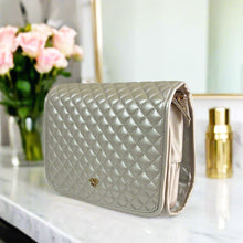 Load image into Gallery viewer, Quilted beige handbag on a marble surface with flowers and a bottle in the background
