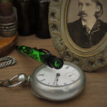 Load image into Gallery viewer, The pen leaning on a silver pocket watch, showing the top disk illustration of Jekyll an Mr. Hyde.
