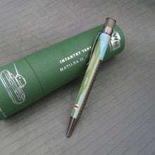 Load image into Gallery viewer, The pen sits side ways on top of the green presentation tube with a gray background.
