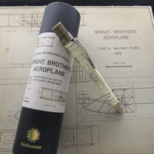 Load image into Gallery viewer, A commemorative writing instrument pen with Wright Brothers Aeroplane printed graphics, resting on top of its cylindrical Smithsonian presentation tube, with vintage airplane blueprint sheets in the background.
