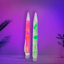 Load image into Gallery viewer, The pink and orange rollerball, and the green and white rollerball, standing upright on a surface against a purple and pink gradient background, with decorative plant leaves at the sides.
