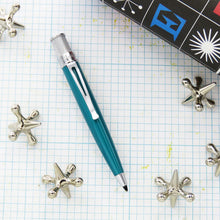 Load image into Gallery viewer, Turquoise ballpoint with decorative objects on a grid background.
