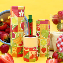 Load image into Gallery viewer, A Strawberry themed green and red pen in its packaging, arranged with bowls and strawberries on a yellow background. 
