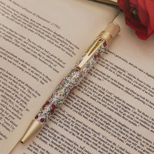 Load image into Gallery viewer, Decorative pen with floral pattern on an open book.
