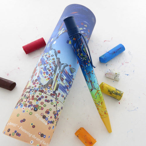 The pen leaning on its matching gift tube with pieces of oil pastel on a white background. 