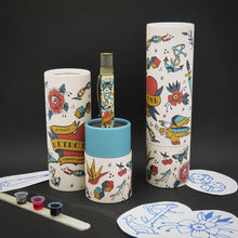 Load image into Gallery viewer, The rollerball pen arranged with the gift tubes, some tattoo designs, and inks on a black background. 
