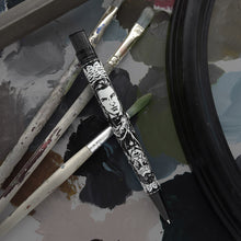 Load image into Gallery viewer, Front view of the Dorian Gray pen resting on top of a set of paint brushes and a paint palette. 
