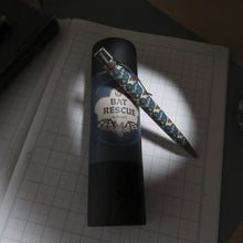 Load image into Gallery viewer, The pen with a bat themed print leaning on its presentation gift tube. 

