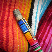 Load image into Gallery viewer, A close-up of the brass brushed clip and twist cap of the pen on top of a colorful pattern.
