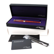 Load image into Gallery viewer, The open black presentation box containing the red with argyle design pen on a purple interior lining, with the brand name S.T. Dupont, along with a pen refill and documents.
