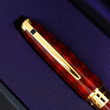 Load image into Gallery viewer, A close-up of the rollerball pen cap, resting diagonally on a purple-lined presentation box.
