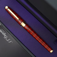 Load image into Gallery viewer, A close-up of the rollerball pen with gold accents, resting diagonally on a purple-lined presentation box.
