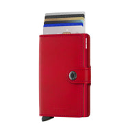 Angled front view of the red mini-wallet with credit cards peeking from the top compartment. It features a button closing strap.