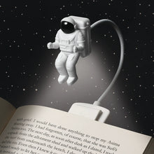 Load image into Gallery viewer, An astronaut-shaped book light attached to a book, with a clip and an adjustable cable.
