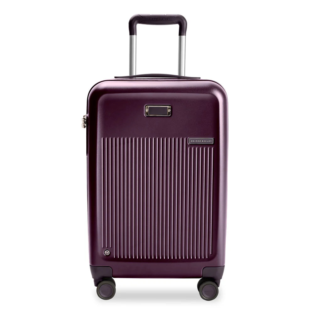 Front view of the plum-colored hard shell suitcase with the telescopic handle extended. It features a  ridged panel, a leather monogram patch, and a small Briggs and Riley logo.