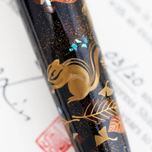 Load image into Gallery viewer, Close up to a chipmunk holding an acorn. It is surrounded by different leaves, gold dust, and bits of blue abalone shell.
