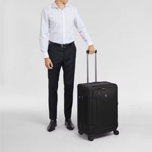 Load image into Gallery viewer, A young man holding the black suitcase by the extended grab handle. 
