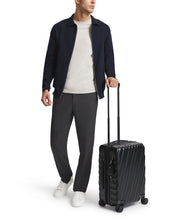 Load image into Gallery viewer, A young man pulling a black suitcase by the telescopic handle on a white background. 
