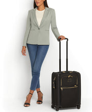 Load image into Gallery viewer, A young woman in light gray blazer and blue jeans pulling a black suitcase by the telescopic handle.
