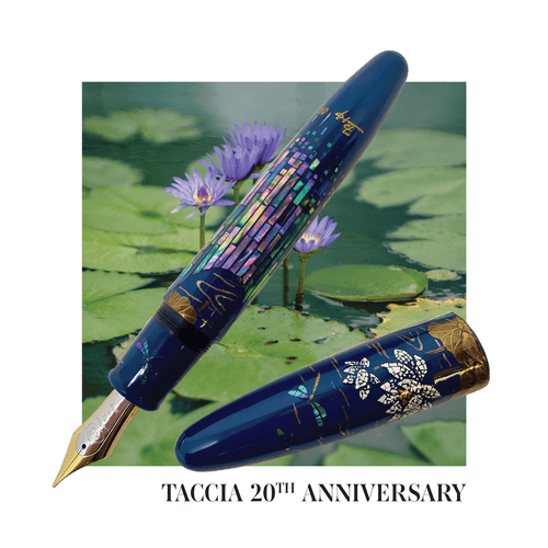 The Taccia Whispering Pond fountain pen with the cap set to the side with a pond with flowers on the background. 