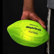 Load image into Gallery viewer, A hand holding the lit up neon green Nightball football on a dark background.

