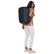 Load image into Gallery viewer, A young woman facing towards the background. She is carrying the blue backpack on the shoulder straps
